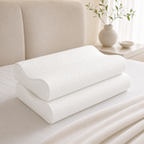 Two white textured memory foam pillows stacked on a white bed sheet in a bright, modern bedroom setting.